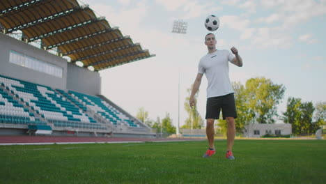 Professional-Male-soccer-player-athlete-on-the-football-field-in-slow-motion-in-sports-equipment-juggles-a-soccer-ball.-A-football-player-with-a-ball-in-the-stadium-near-the-stands